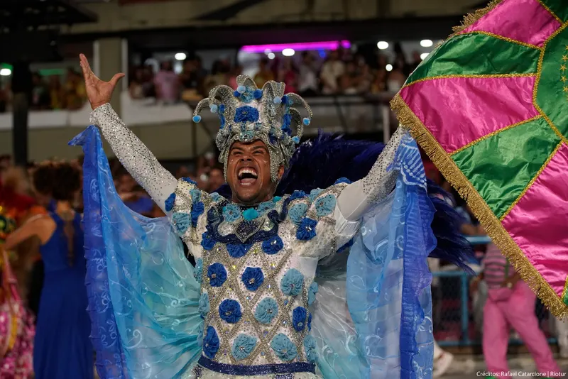 A performer in an ornate blue and silver costume with arms raised in celebration