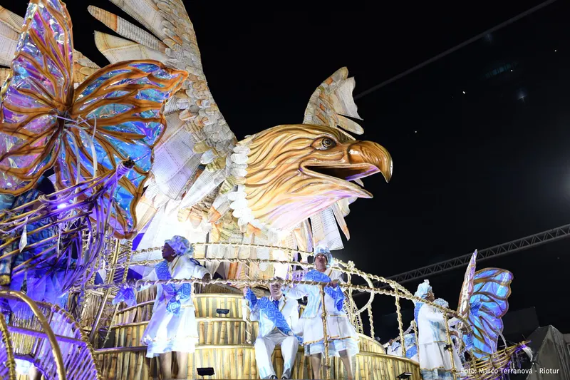 A silver float shaped like a giant eagle with butterflies, lit up at night