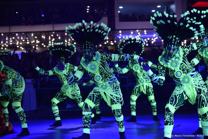 Dancers in glowing neon-green costumes performing under blue light